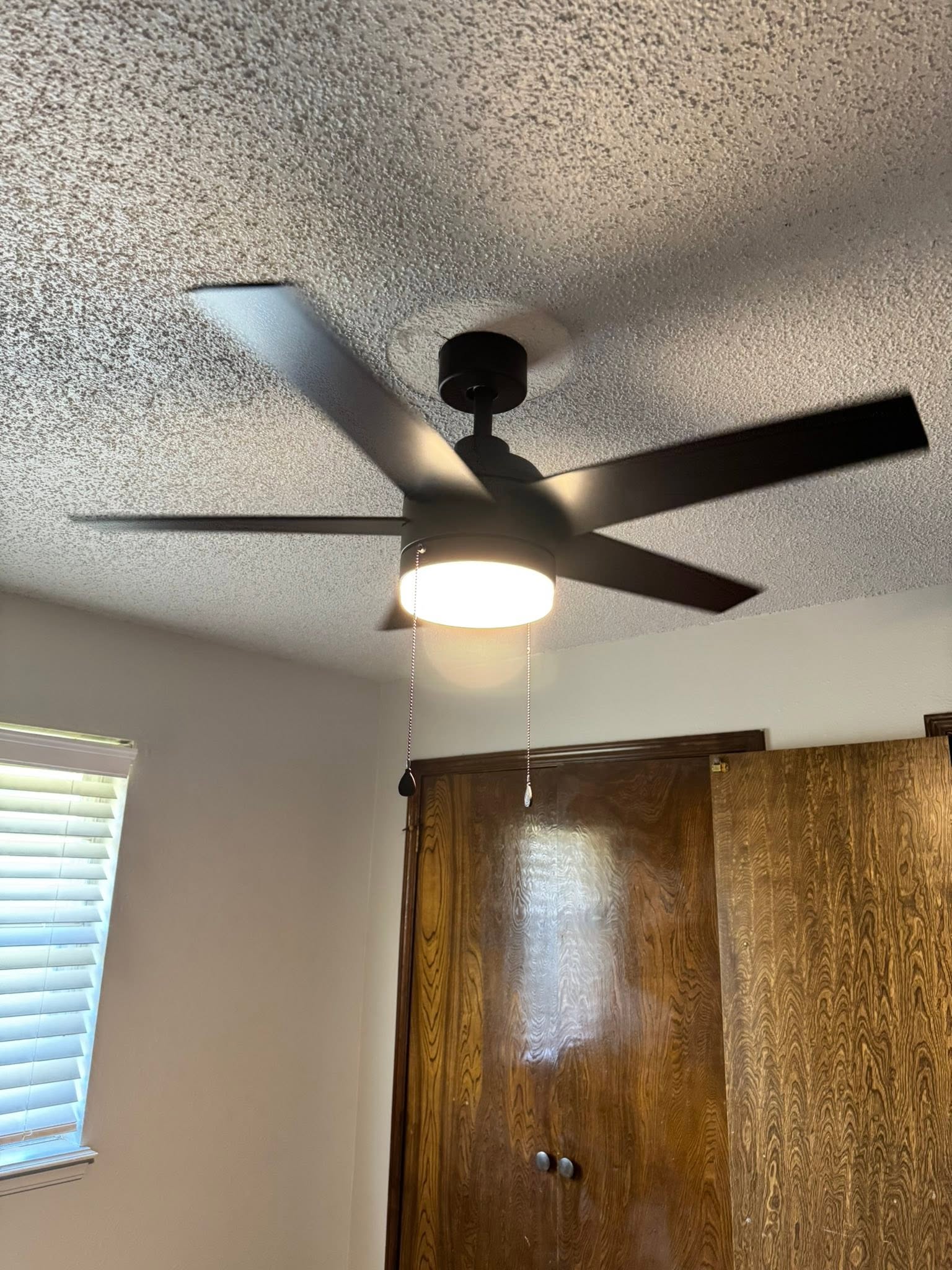 Black ceiling fan with a light kit installed on a textured ceiling